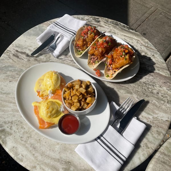 White Maple Café's salmon eggs benedict with home fries and three fish tacos on a marble table.