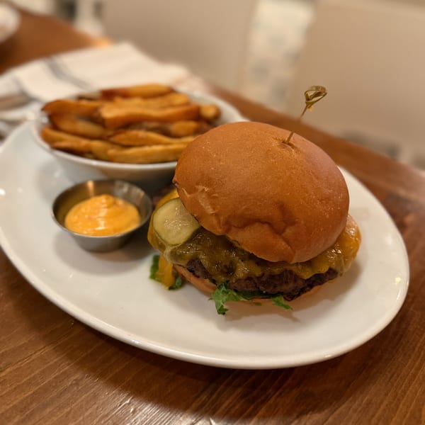 A White Maple Café burger with melted cheese, pickles, and lettuce, served with fries and dipping sauce.