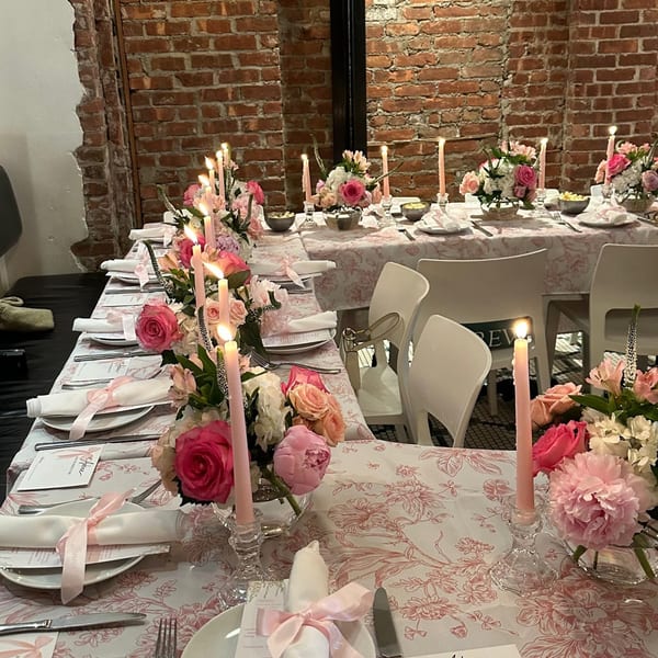 A long table set for a special event with pink floral tablecloths, candles, and flower arrangements.