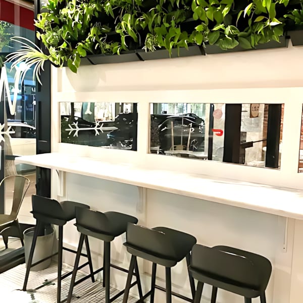 A modern bar area with black stools, a white counter, and a lush green plant wall.
