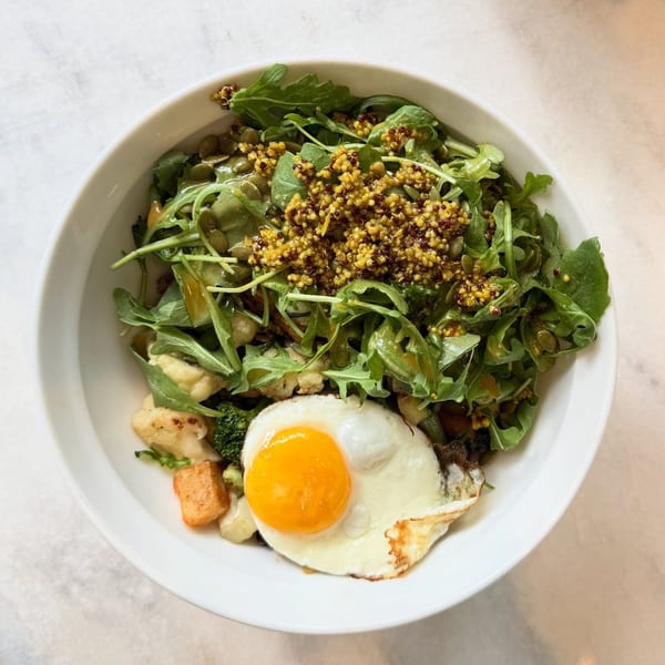 A White Maple Café breakfast bowl with arugula, quinoa, pumpkin seeds, roasted vegetables, and a fried egg.