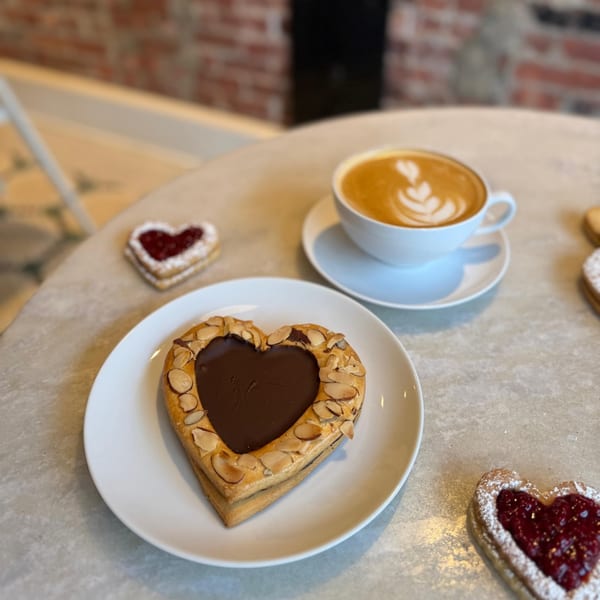 Heart-shaped pastries with chocolate and jam fillings, alongside a latte with foam art on a table.