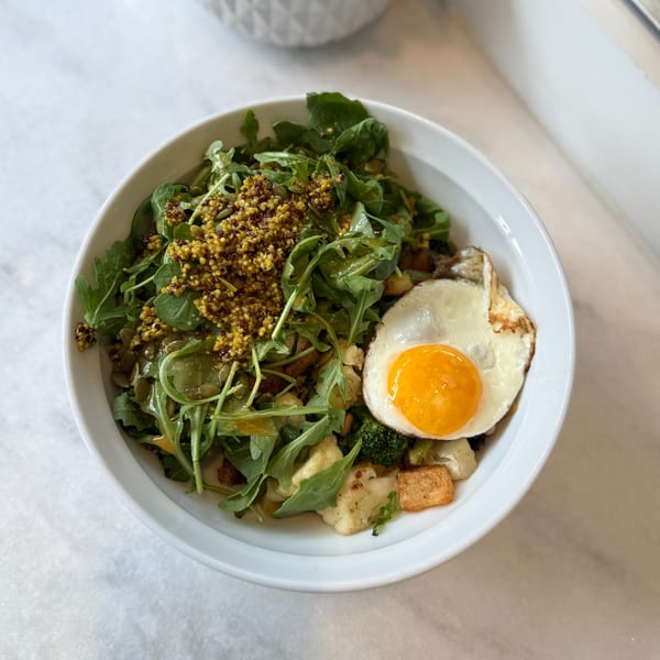 A White Maple Café breakfast bowl with arugula, quinoa, vegetables, and a fried egg.