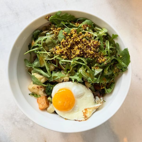 A White Maple Café breakfast bowl with arugula, quinoa, pumpkin seeds, vegetables, and a fried egg.