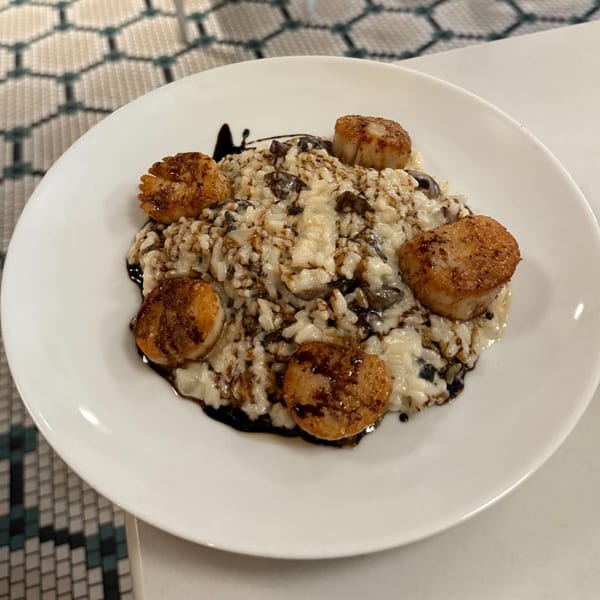 Creamy mushroom risotto with five perfectly seared scallops and a balsamic drizzle on a white plate.