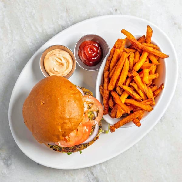 White Maple Café's burger with tomato, onion, lettuce, and a side of sweet potato fries and sauces.