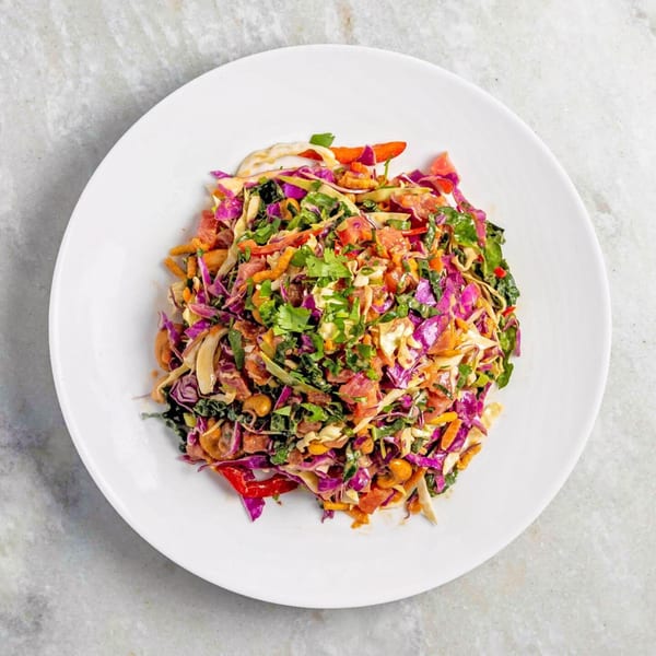 Overhead view of a colorful salad with purple cabbage, green herbs, and red peppers on a white plate.