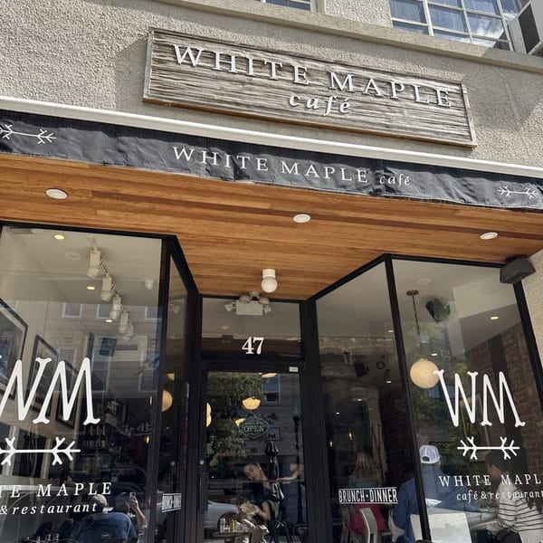 The exterior of White Maple Cafe, featuring its sign, awning, and glass storefront with patrons inside.
