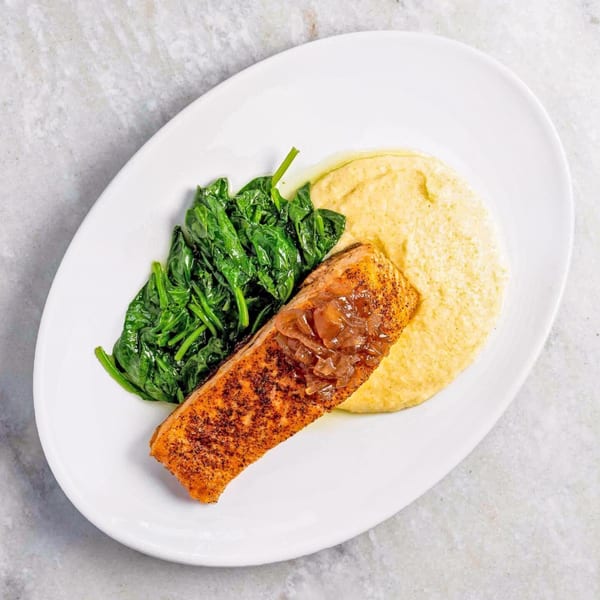 Seared salmon with caramelized onions, a side of creamed spinach, and polenta on a white plate.