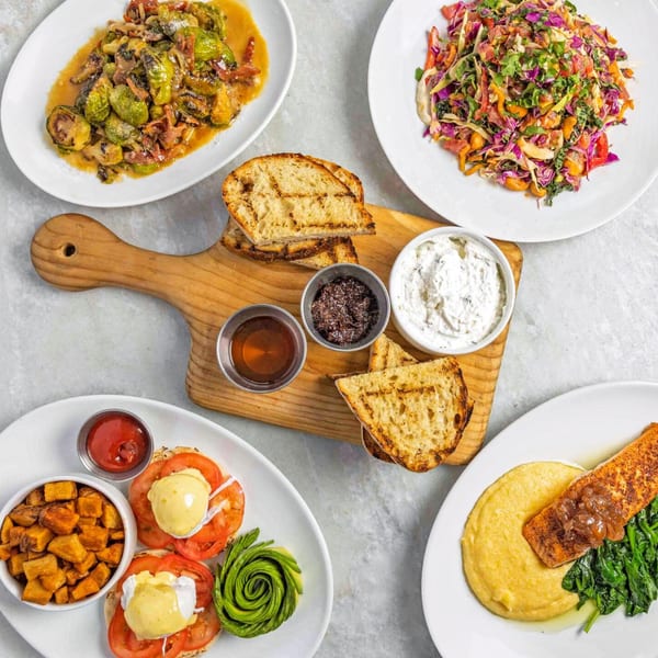 Overhead view of five American dishes, including Brussels sprouts, salad, eggs Benedict, salmon, and grilled bread.