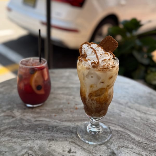 Two drinks on a marble table: a red fruit punch and an iced coffee with whipped cream and a cookie.