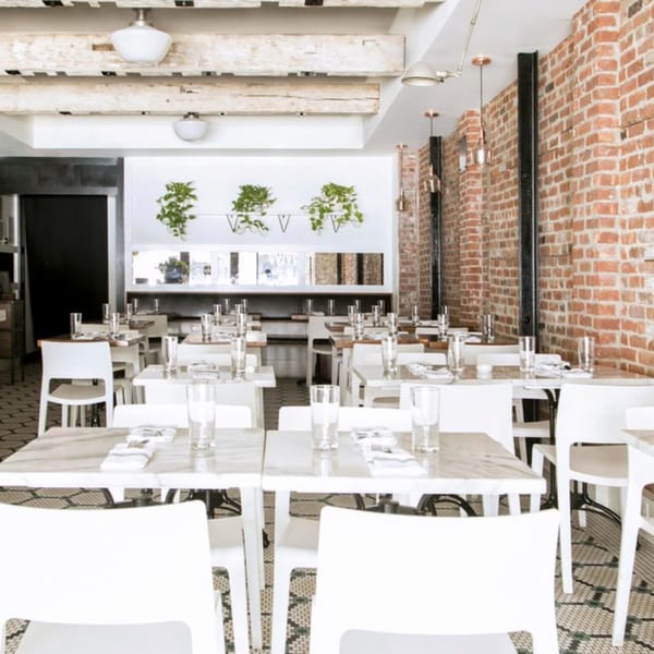 Bright, modern dining room at White Maple Café with white chairs, marble tables, and exposed brick.
