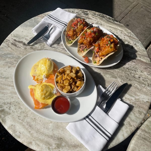 Eggs Benedict with smoked salmon, home fries, and three shrimp tacos on a marble table.