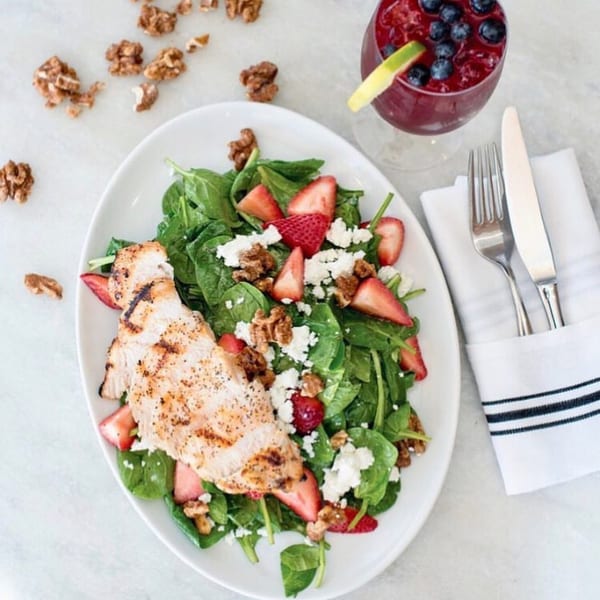 Grilled chicken and spinach salad with strawberries, feta, and walnuts, alongside a berry drink.