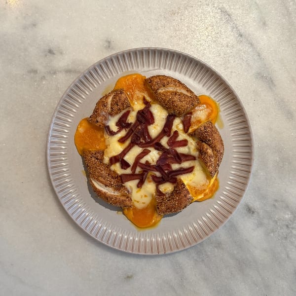 A sesame bagel with melted cheese and strips of pastrami on a grey plate.