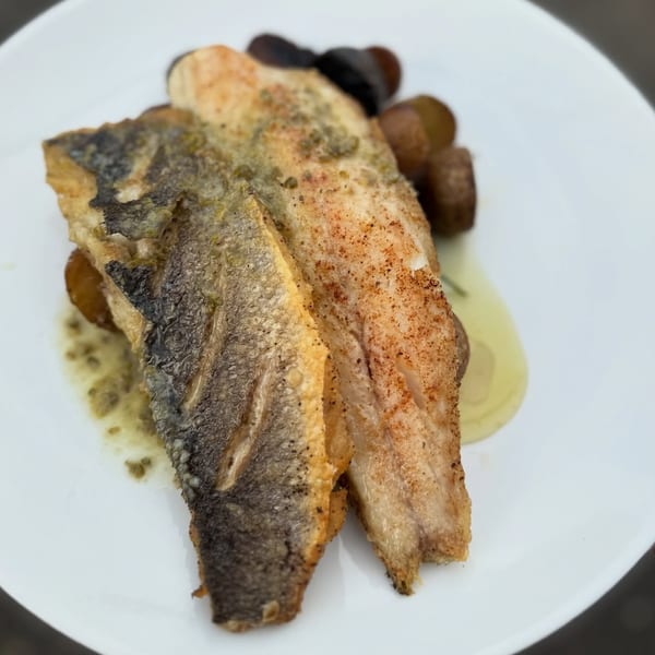 Two fillets of pan-seared fish with crispy skin, drizzled with sauce, served on a white plate.