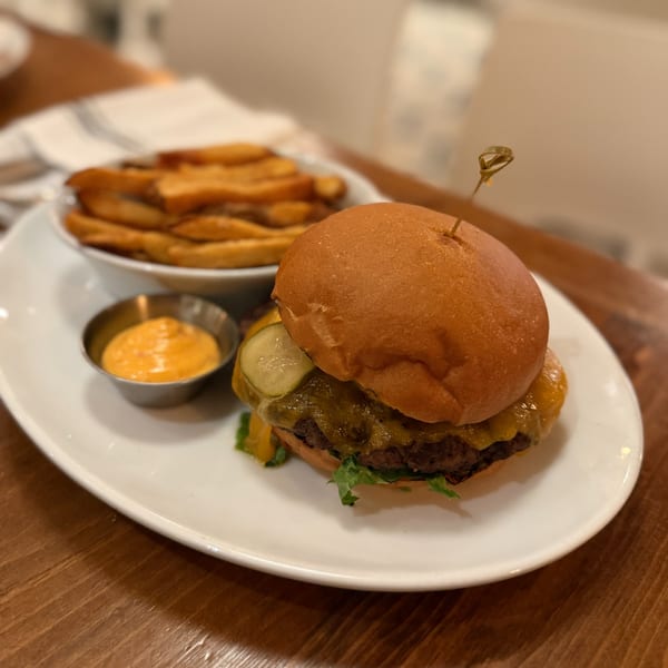 A White Maple Café cheeseburger with pickles, lettuce, fries, and dipping sauce on a white plate.