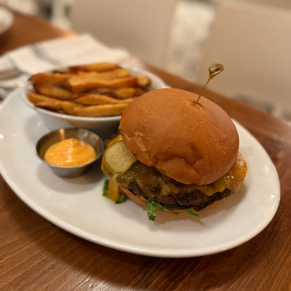 A White Maple Café cheeseburger with pickles, lettuce, fries, and dipping sauce on a white plate.